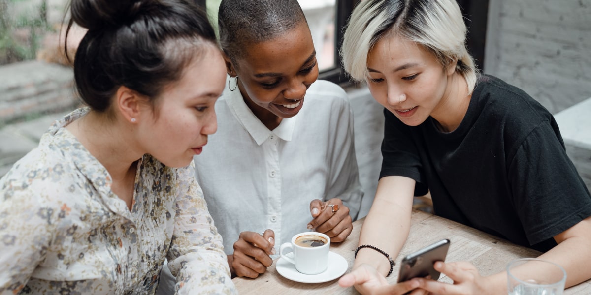Three UX designers gathered at a table, looking at recent project results on a phone