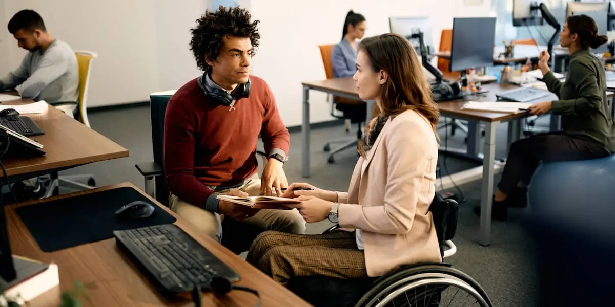 A data analyst in a wheelchair talking to a product manager in an office.