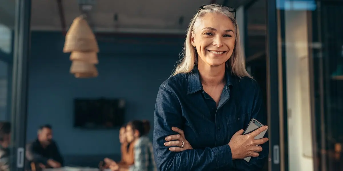 A woman who successfully graduated from a coding bootcamp stands in an office smiling at the camera.