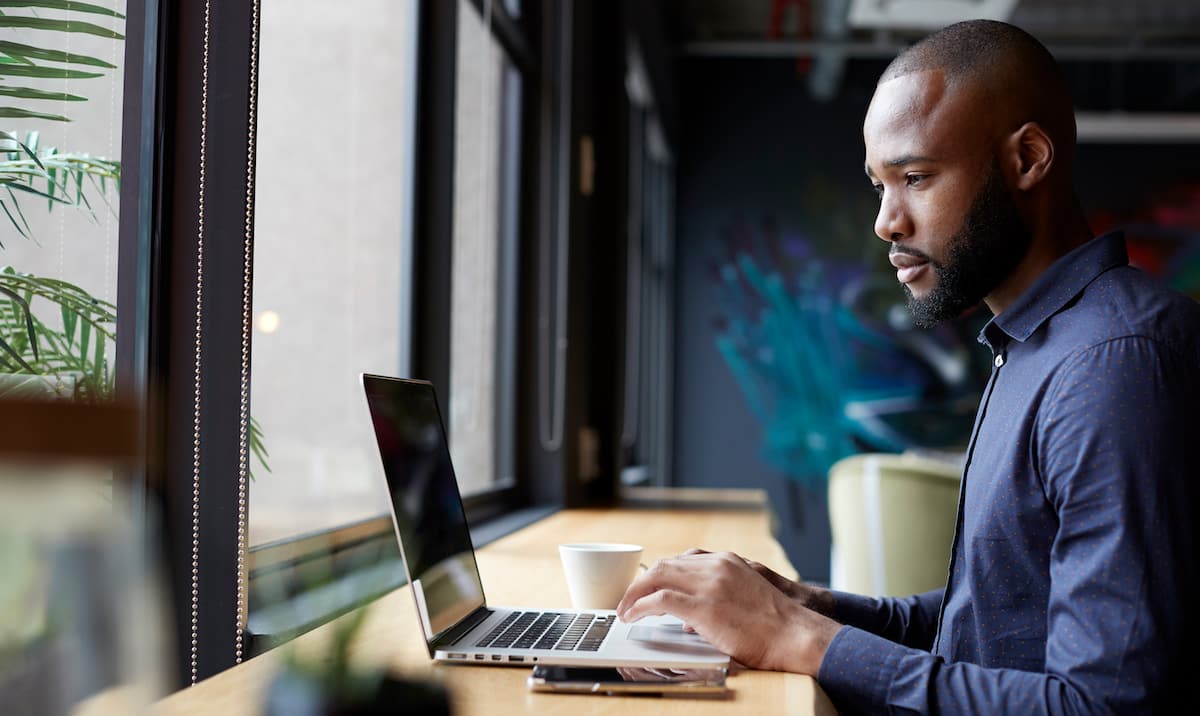 A remote product manager types on his computer with a coffee cup beside him.