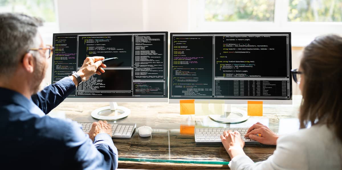 Two people doing pair programming work at code on their screens.