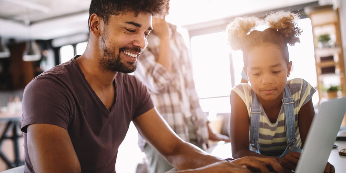 An aspiring UX designer working at a laptop while his child looks on