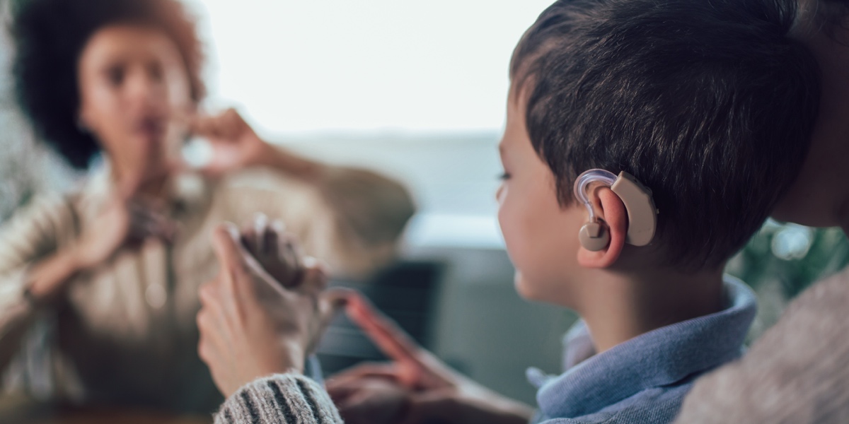 UX Trends 2021: Accessibility and Inclusion A child wearing a hearing aid, working across a table from an educator