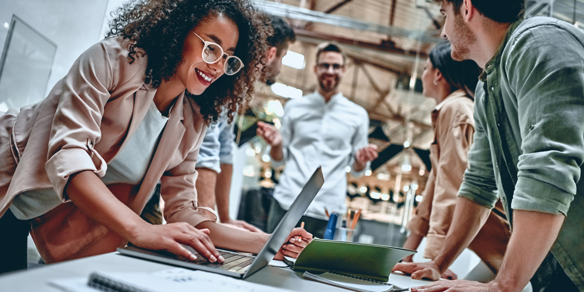 A UX instructor standing at a table with her students, engaged in a discussion