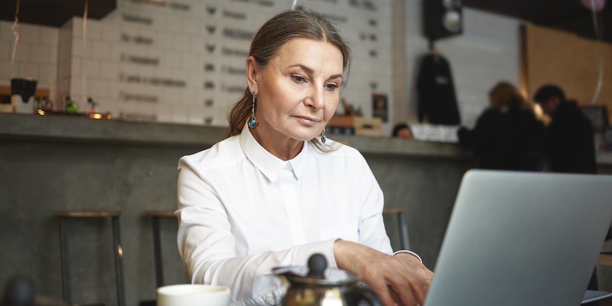 Woman working as a web developer sitting in a café looking at a laptop screen