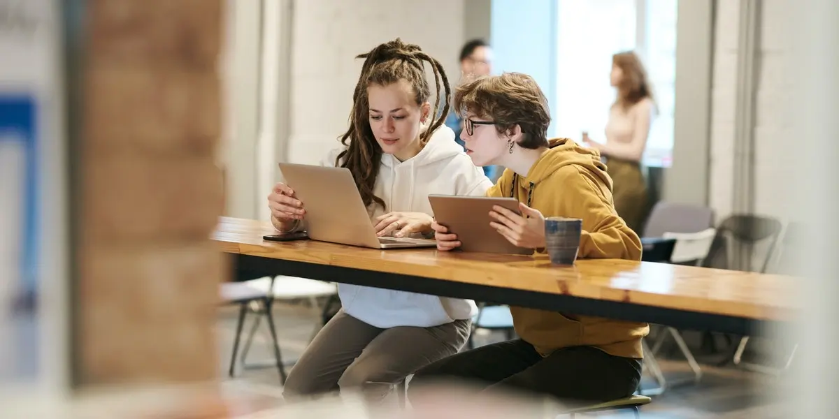 Two coding students sit at a table on a laptop and a tablet learning what is CSS.