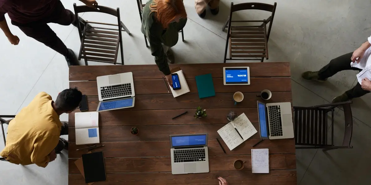 A team of web developers at a startup with their laptops sitting on a large table in an office.