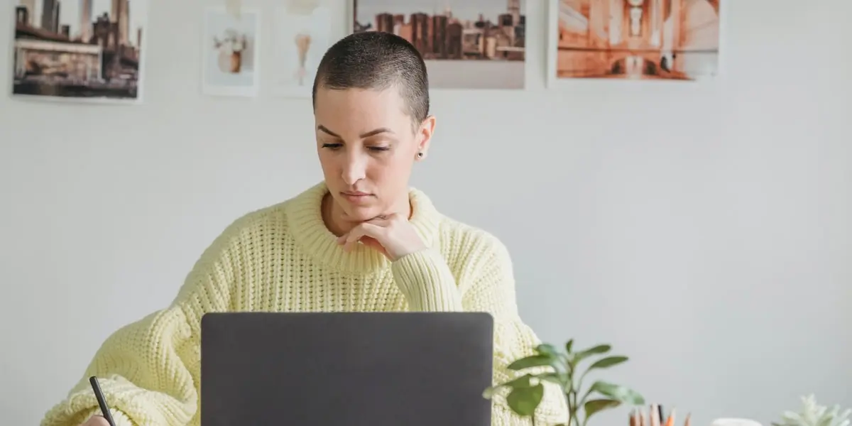 A UX designer working from home at a desk with a laptop, surrounded by plants