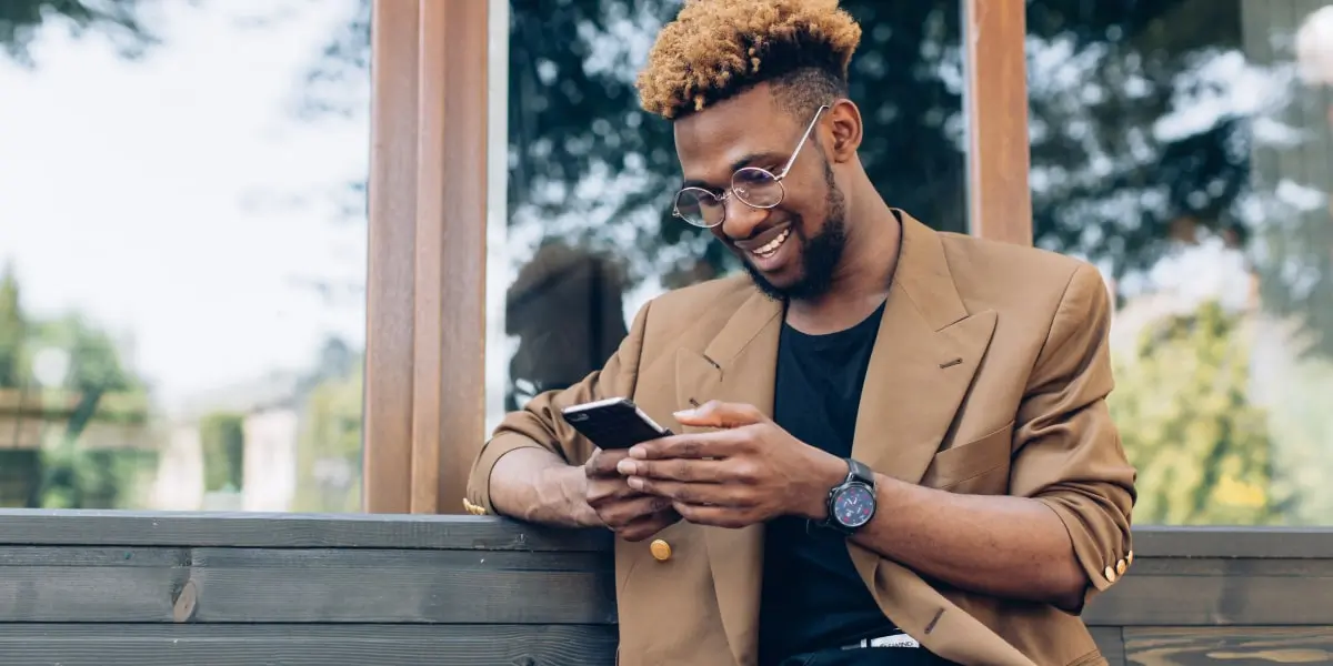 A person sitting on a bench, holding a smartphone, smiling