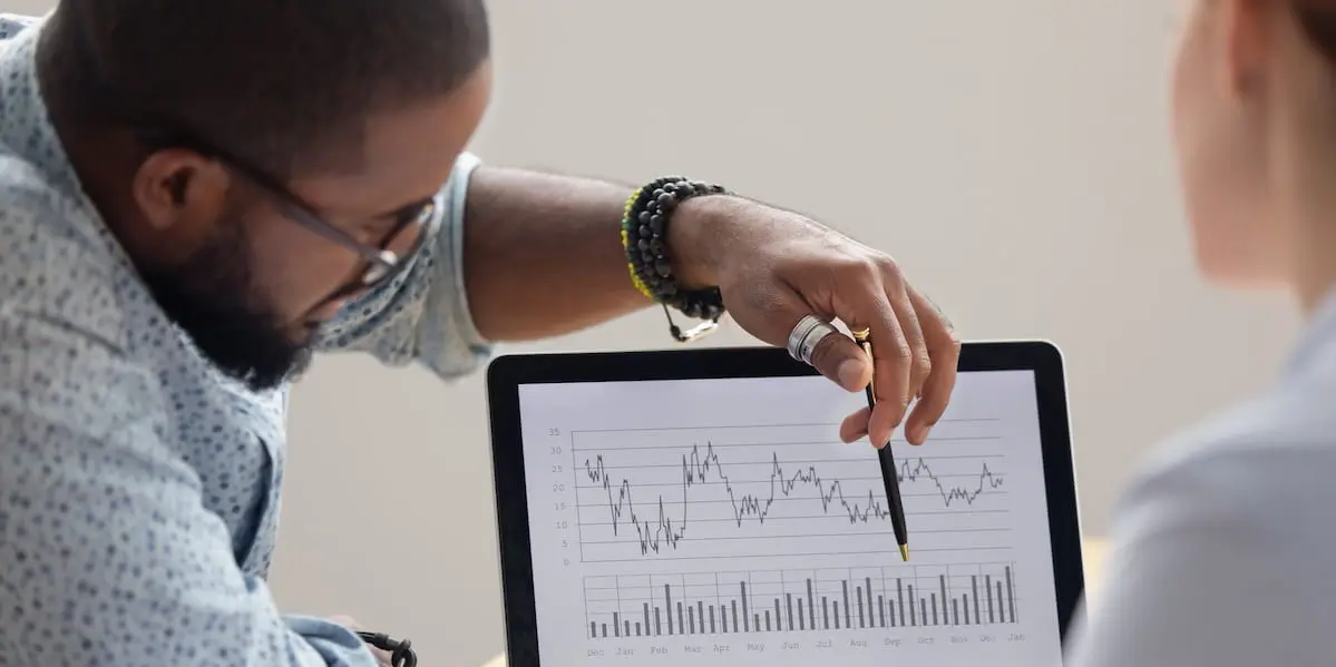 A data analyst explains a graph on a laptop to a woman. He became a data analyst with no experience.