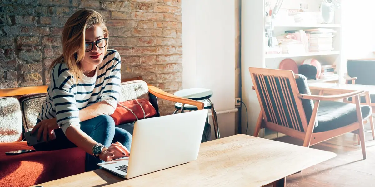 A woman sitting on a sofa in a cafe, working on her laptop