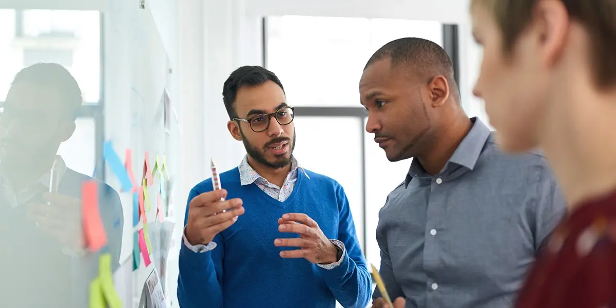 Three designers standing at a whiteboard discussing CX (customer experience)