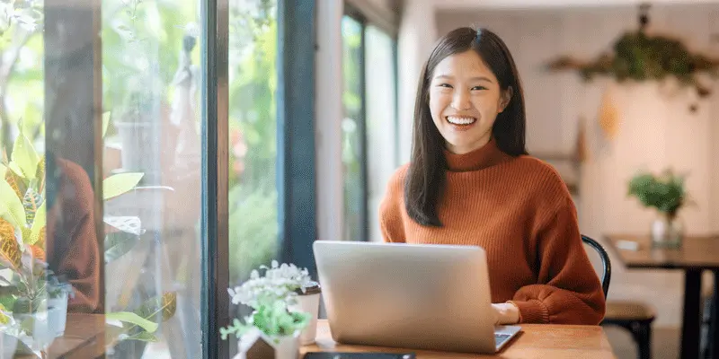 A UX designer sitting in her living room, working at a laptop and smiling