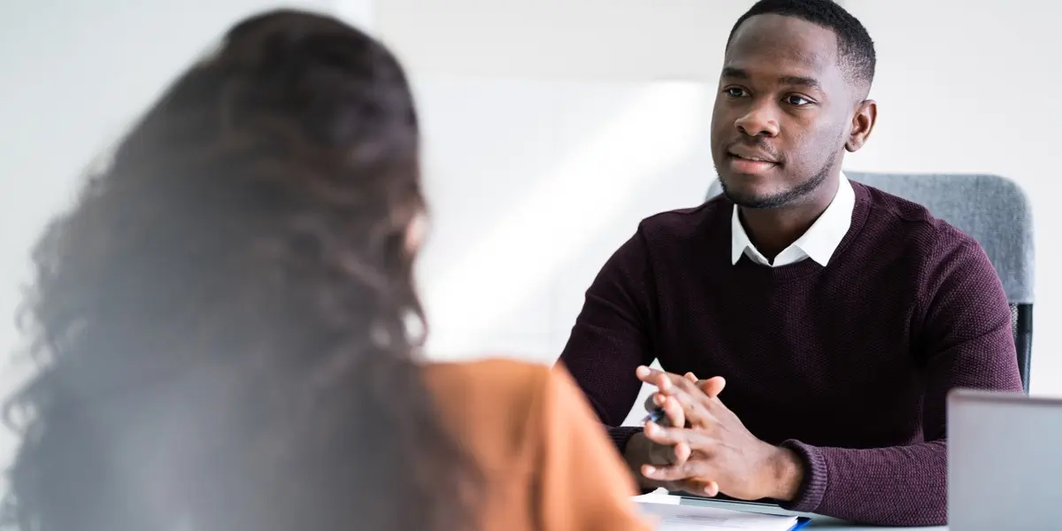 Two people sitting opposite each other at a desk, having a conversation