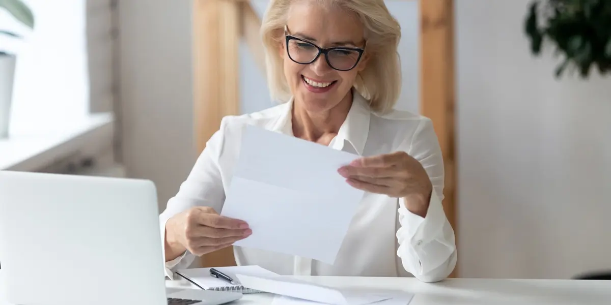 A newly qualified UX designer sitting at a desk, smiling and holding her UX design certification