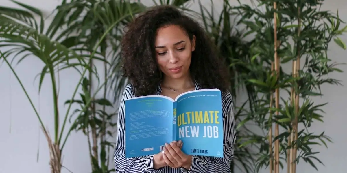 An asiring UX designer sitting next to some plants, reading a book