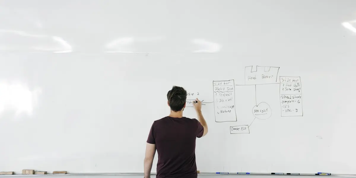 A new uUX designer standing at a whiteboard, drawing wireframes with their back to the camera