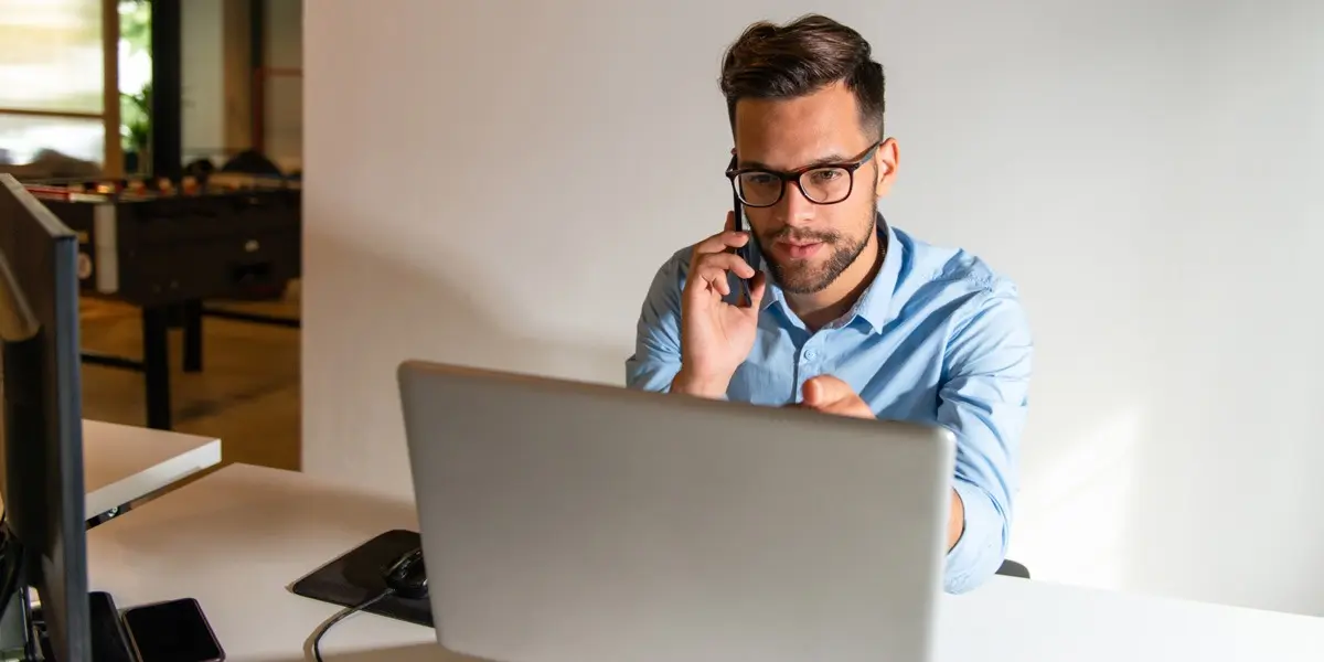 A data analyst looking at a laptop, talking on the phone