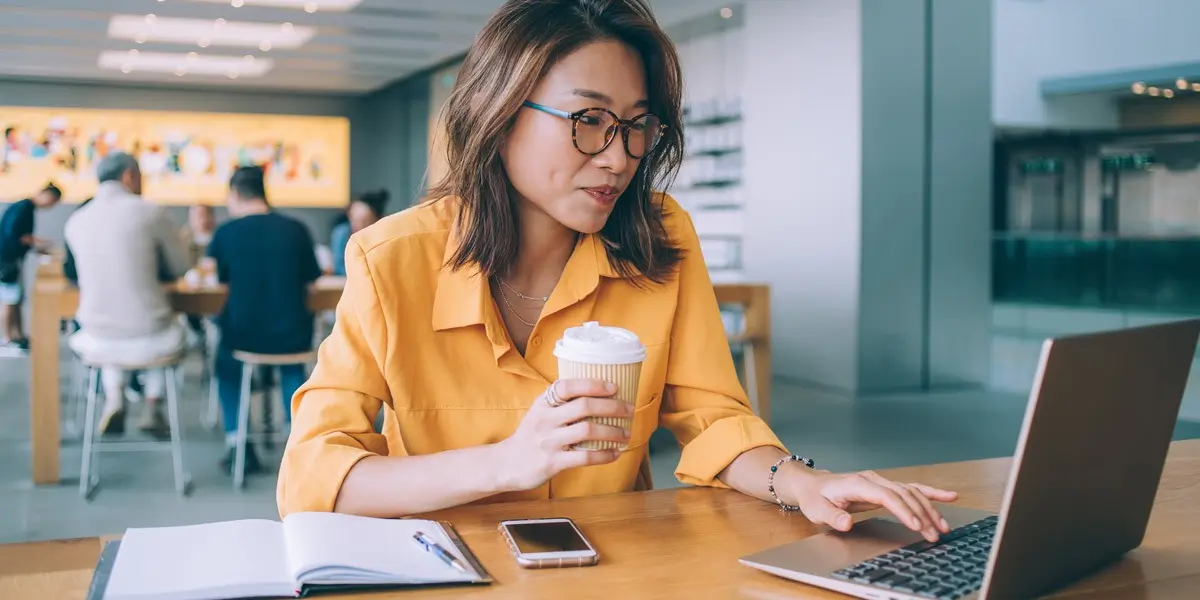 A data analyst holding a cup of coffee, working on a laptop