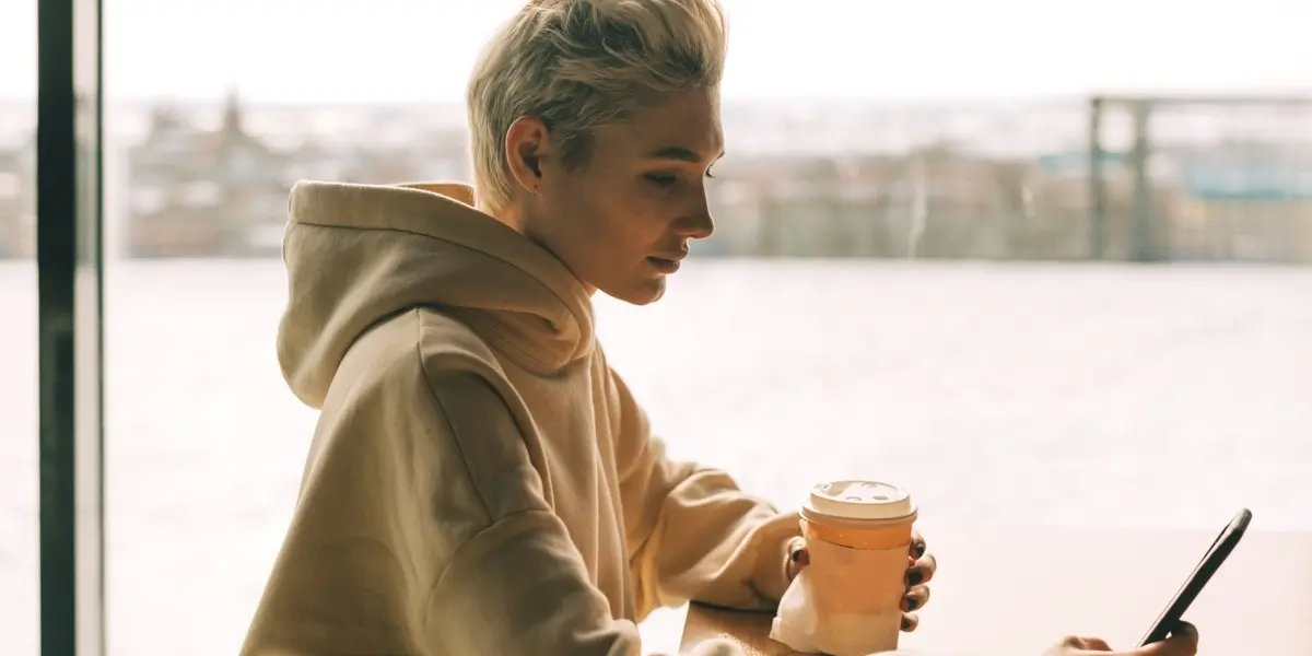 An androgynous person sitting at a table near a window, looking at their laptop