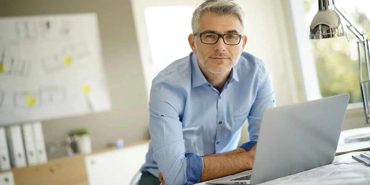 A designer smiling, sitting at a desk with a laptop