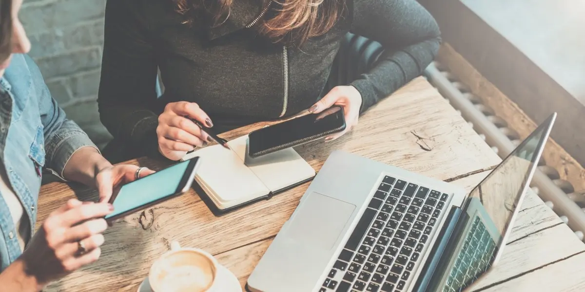 Overhead view of a UX designer working at a desk with a notebook, phone, and laptop