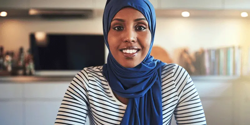 A web developer in a headscarf working from home looks at the camera.