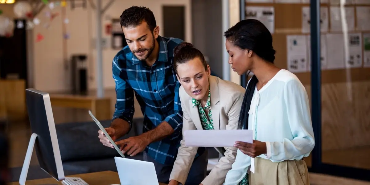 Three UX designers gathered around a computer, discussing a project