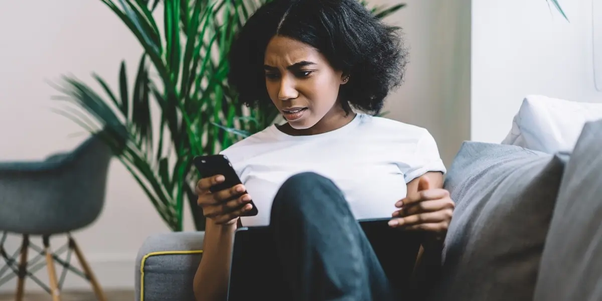 A person sitting on a couch at home, looking at their phone with frustration