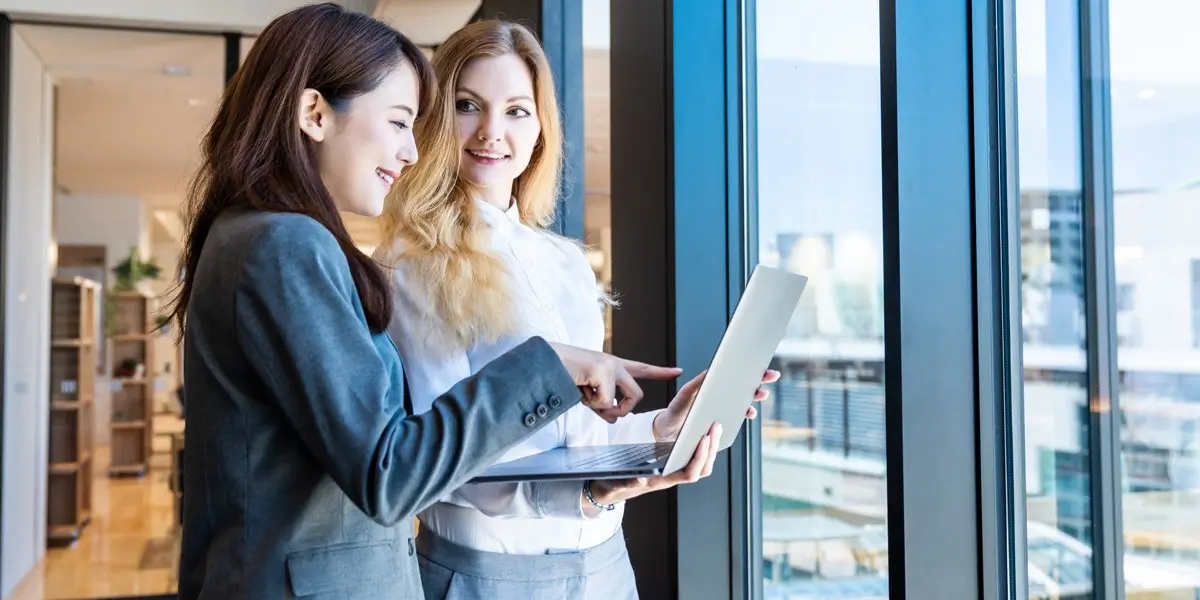 Two data analysts standing by a window, looking at a laptop