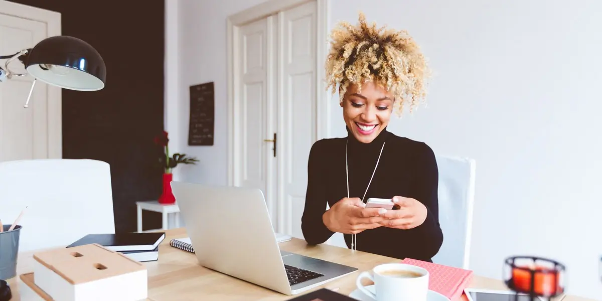 A UX designer sitting at a desk with her laptop, looking at her phone