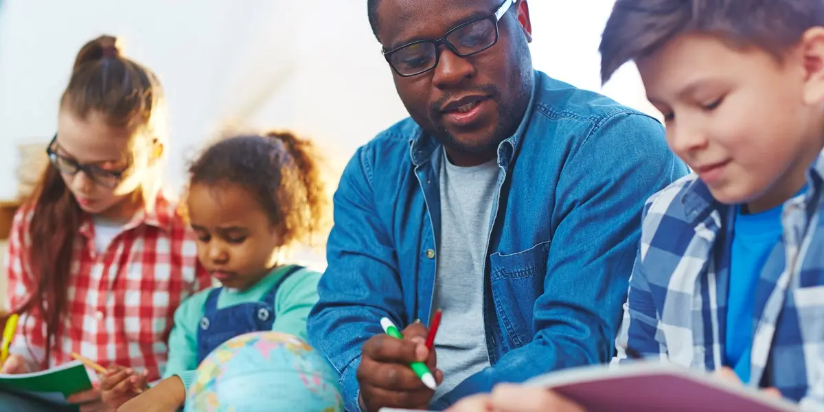 A teacher sitting with three students, helping them with their studies