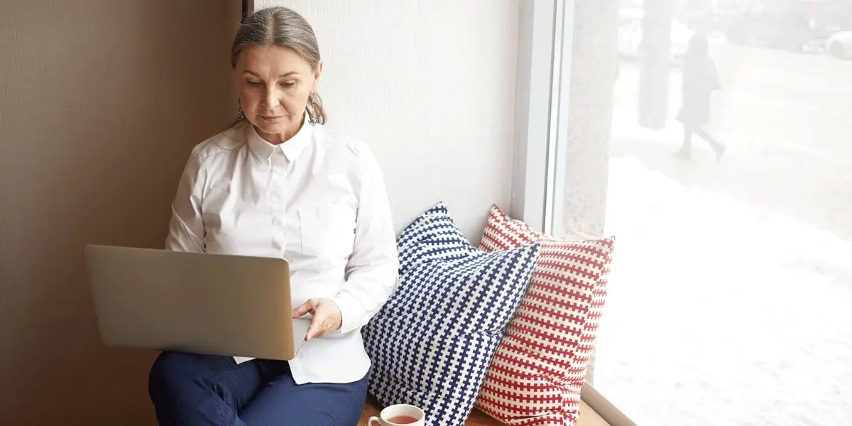 A UI designer sitting next to a window, working on a laptop