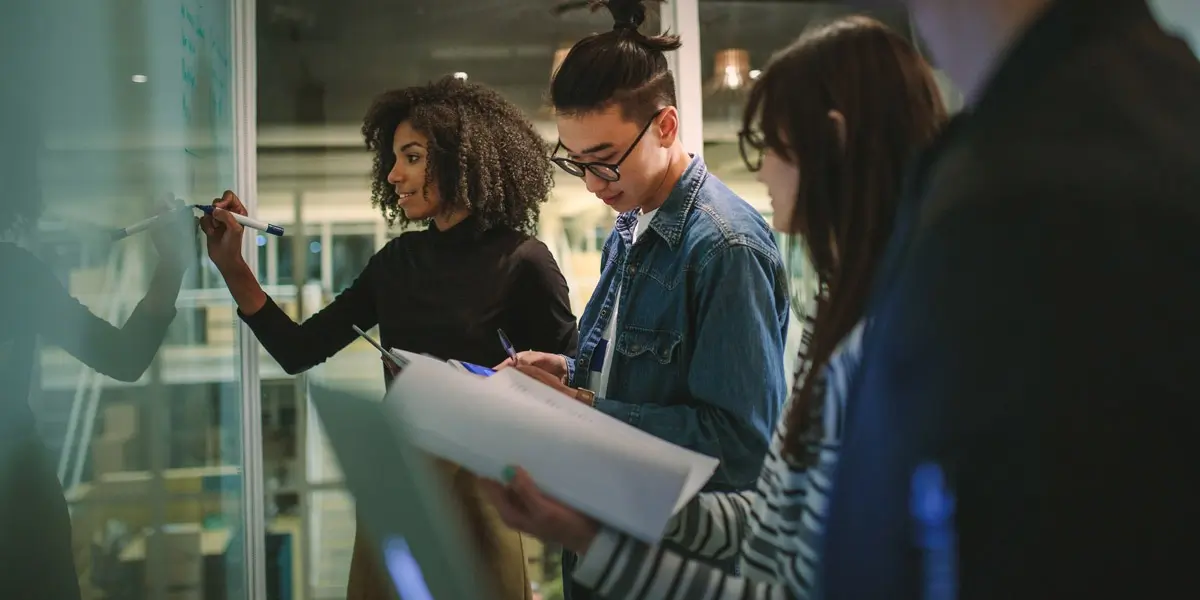 A group of aspiring UX designers, standing at a work space and looking at notes