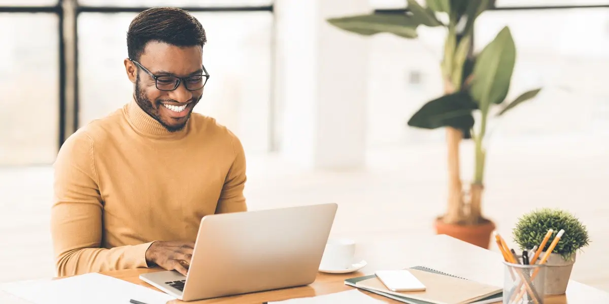 A man works in a bright room learning UX designer skills on a laptop.