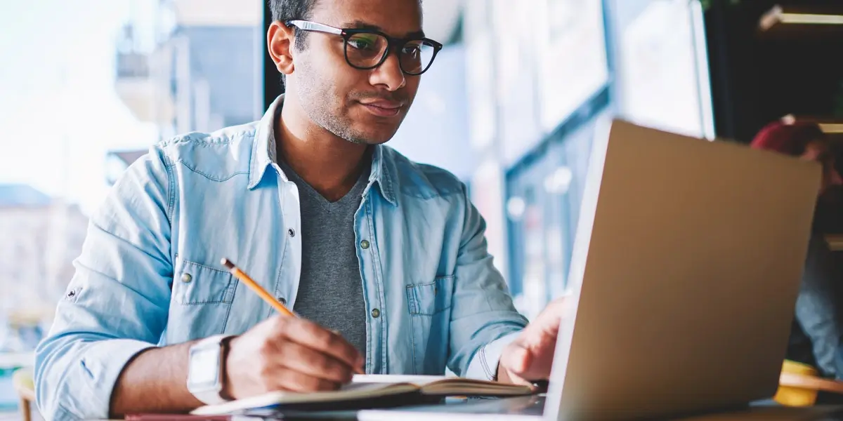 A UX designer sitting at a desk with a laptop, pencil, and paper, working on a prototype