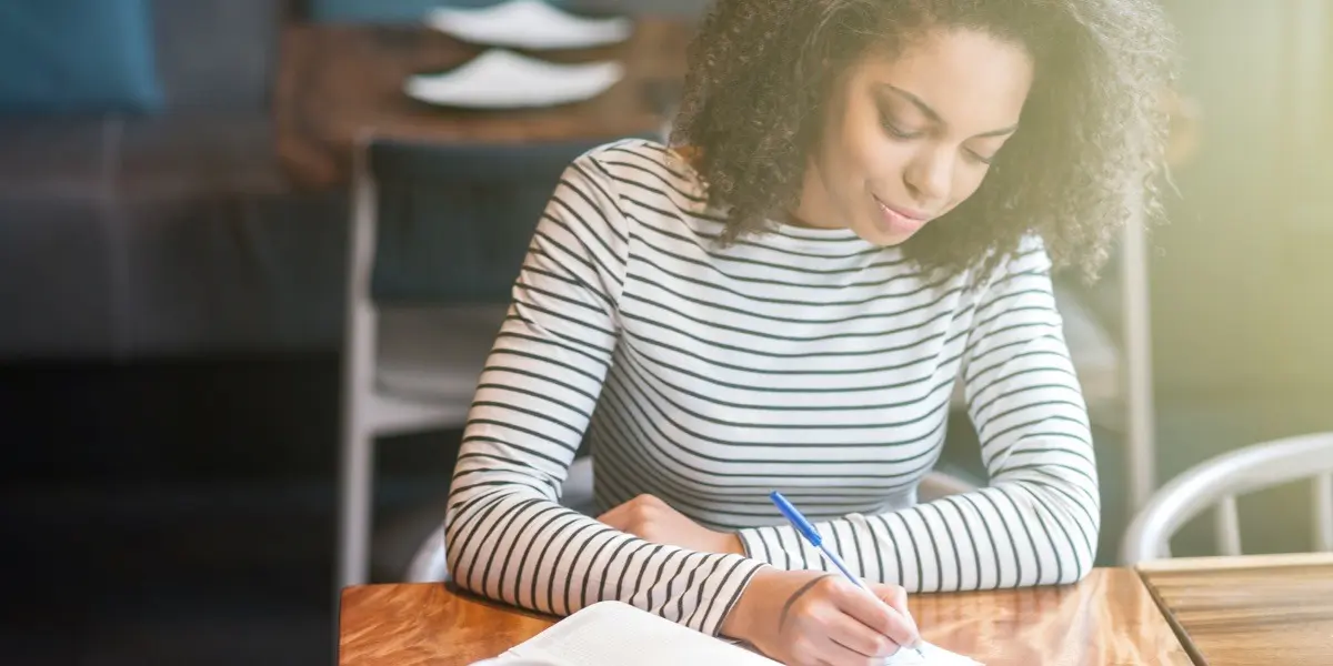 A UX writer sitting in a cafe taking notes on a pad of paper