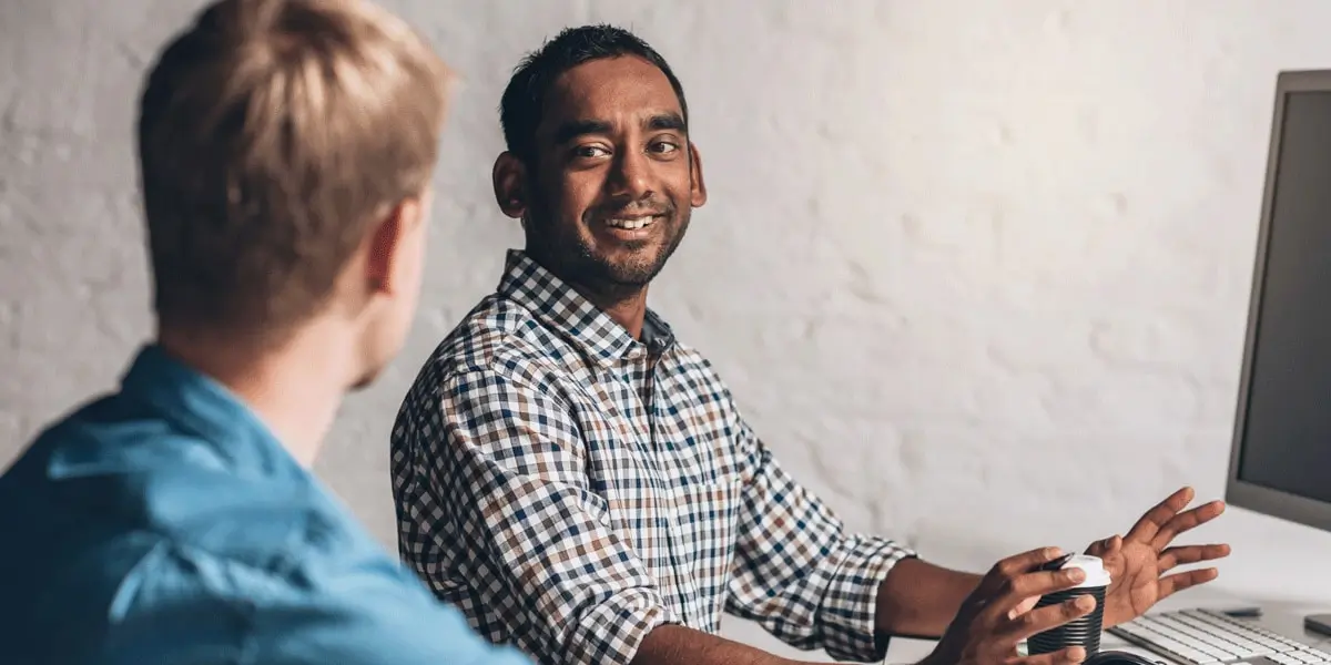 A JavaScript developer explains some code on his computer to a colleague in an office.