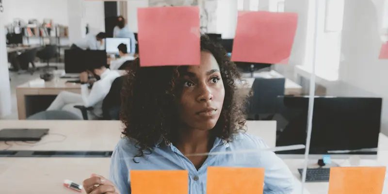 A designer standing behind a glass wall, looking at ideas posted on sticky notes