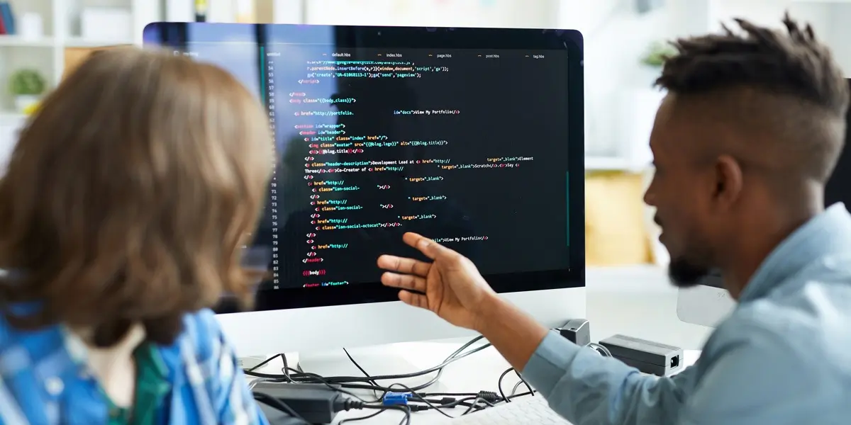 Two data analysts looking at code on a computer screen