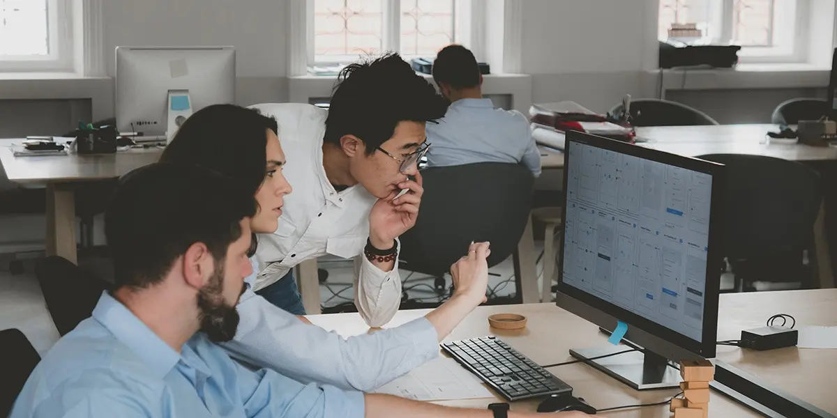 three designers in their office, gathered around a computer to look at a project