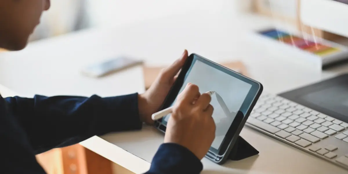 A designer sitting at a desk, holding a stylus to working on a free wireframe tool on a tablet