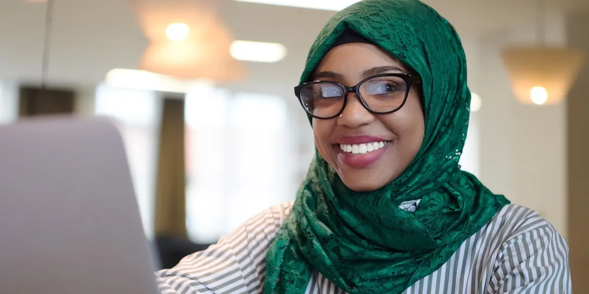 A data analyst smiling at the camera, working on a computer