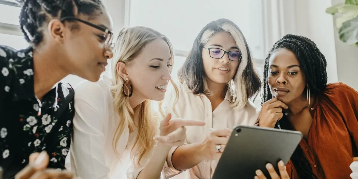 Group of women gathered around a tablet, discussing ideas