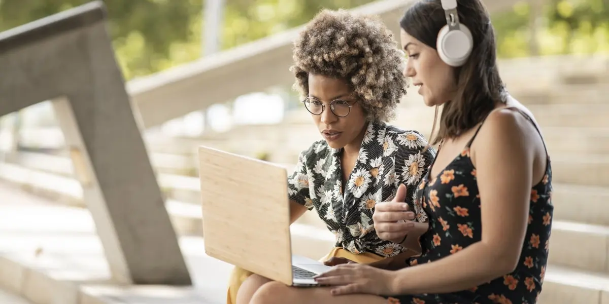 Two attendees of a web development bootcamp sit outside and look at a laptop.