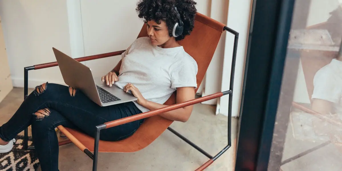 A UI designer sitting in a chair wearing headphones, looking at a laptop