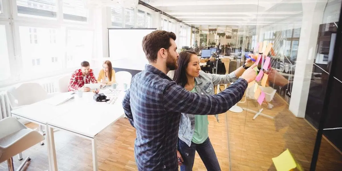 Two web developers plan work in a meeting room in a startup office.