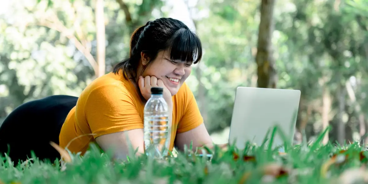 A data analyst laying on the grass, looking at a laptop screen