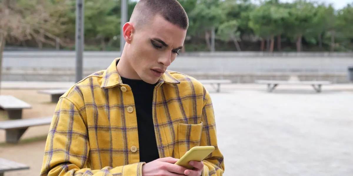 A genderqueer person standing in a park, working on their phone