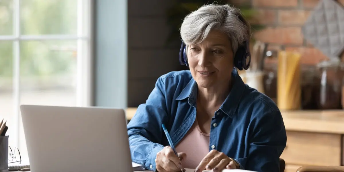 Elderly woman sits at a kitchen table taking free web development courses on her laptop.